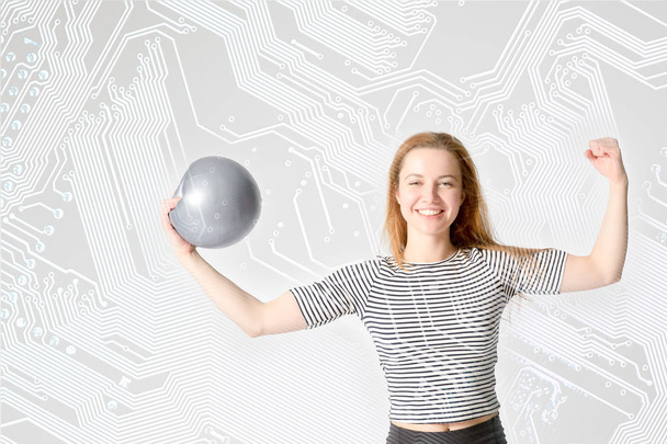 jonge vrouw atleet met sterke biceps houdt de bal in zijn hand op een computer printplaat achtergrond. Concept van onderwijs - een sterke sport-informatica. - Foto, afbeelding