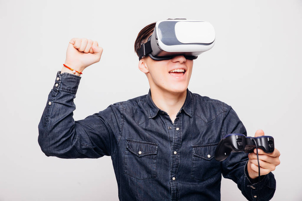 Jeune homme jouant à des jeux vidéo avec casque de réalité virtuelle et joystick ou conduisant avec télécommande
. - Photo, image