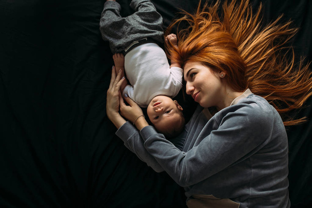 Ευτυχισμένη μητέρα με το μωρό μαζί ξαπλωμένος στο κρεβάτι - Φωτογραφία, εικόνα