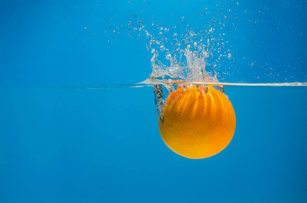 Orange splashing in water with blue background - Fotó, kép