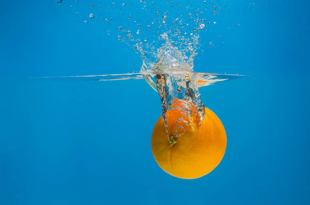 Orange splashing in water with blue background - Foto, Imagen