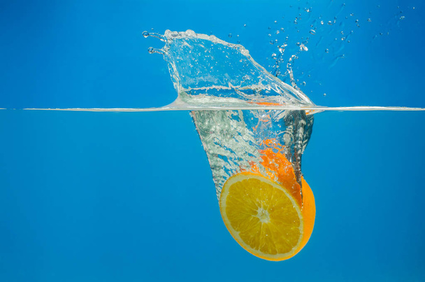 Orange splashing in water with blue background - Foto, afbeelding
