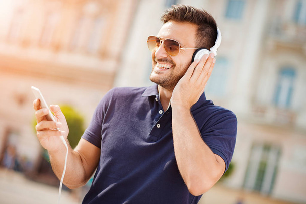 Joven hombre atractivo está sonriendo mientras usa auriculares
 - Foto, Imagen
