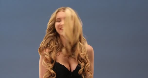 Καμπύλες σέξι ξανθιά γυναίκα με όμορφα μακριά σγουρά μαλλιά θέτοντας σε μαύρο σουτιέν - Πλάνα, βίντεο