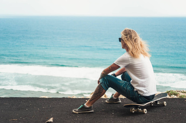 junger Mann blonde Skater sitzt vor erstaunlichen Meerblick - Foto, Bild