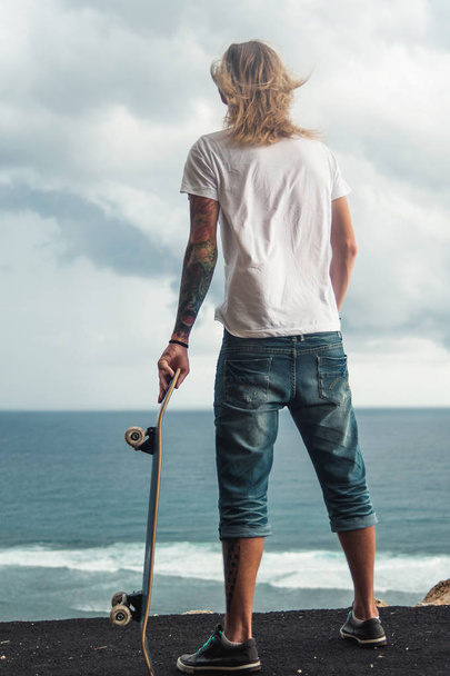 Back view of a skater standing on a high in front of amazing ocean view - Fotoğraf, Görsel