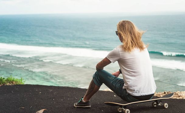  Young man blonde skater sitting in front of amazing ocean view - Foto, Imagen