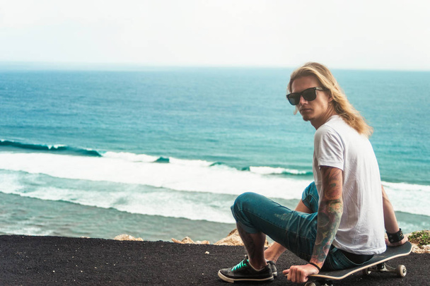  Young man blonde skater sitting in front of amazing ocean view - Φωτογραφία, εικόνα