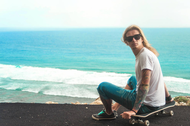 Young man blonde skater sitting in front of amazing ocean view - Foto, immagini
