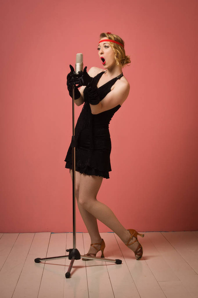 Όμορφη ηθοποιός στο μαύρο φόρεμα κλασικο τραγούδι με μικρόφωνο - Φωτογραφία, εικόνα