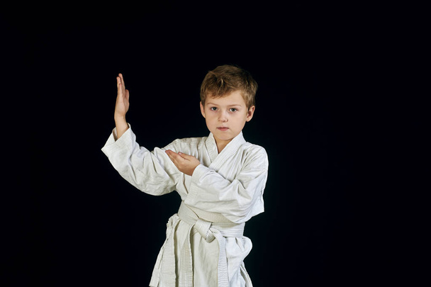 Młody chłopak w kimono pokazuje sztuki walki na czarnym tle - Zdjęcie, obraz