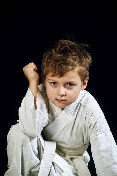 Young boy in kimono shows the martial arts on a black background - Photo, Image