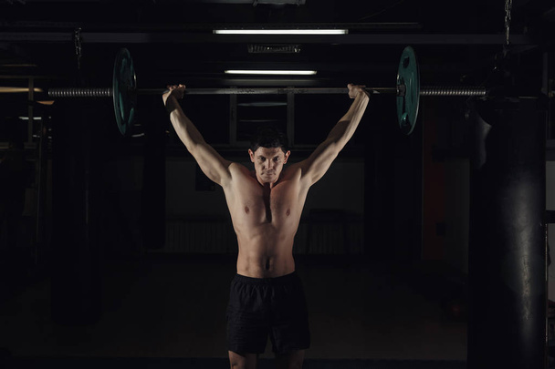 Muscular man at a crossfit gym lifting a barbell. - Foto, Bild