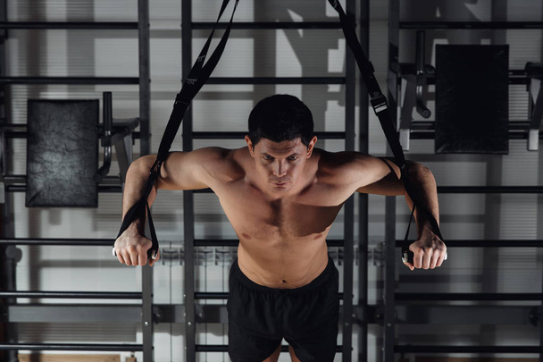 Hombre atractivo hace Crossfit Empuje Ups con correas de fitness en el estudio del gimnasio
. - Foto, Imagen