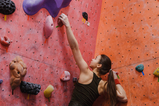 Joven mujer musculosa deportiva subiendo a la pared de roca en el gimnasio, vista trasera. Concepto de bouldering profesional
 - Foto, imagen