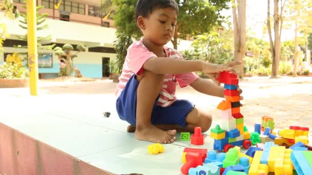 Blokuje mały ładny chłopiec azjatyckich gry z tworzywa sztucznego budynku w parku - Materiał filmowy, wideo