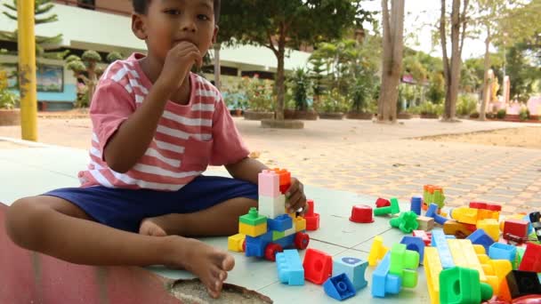 Kis aranyos ázsiai fiú játék-val műanyag épület márványtömbök a parkban - Felvétel, videó