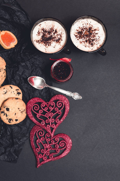 Romantik kahvaltı. İki bardak kahve, cappuccino çikolatalı kurabiye ve bisküvi siyah tablo arka plan üzerinde kırmızı kalpler yakınındaki ile. Sevgililer günü. Seviyorum. Üstten Görünüm.  - Fotoğraf, Görsel