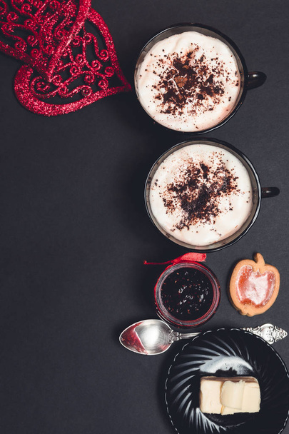 Romantik kahvaltı. İki bardak kahve, cappuccino çikolatalı kurabiye ve bisküvi siyah tablo arka plan üzerinde kırmızı kalpler yakınındaki ile. Sevgililer günü. Seviyorum. Üstten Görünüm. - Fotoğraf, Görsel