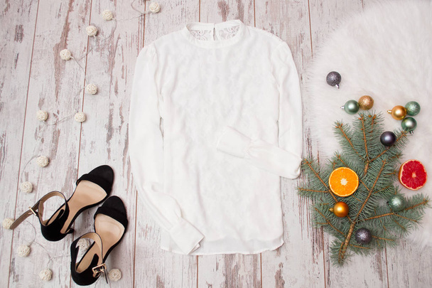 White blouse and black shoes on a wooden background, Christmas balls on fir branch. Fashionable concept, top view - Photo, Image