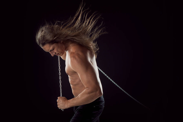 Young man with long hair dragging something behind him. Strong. - 写真・画像