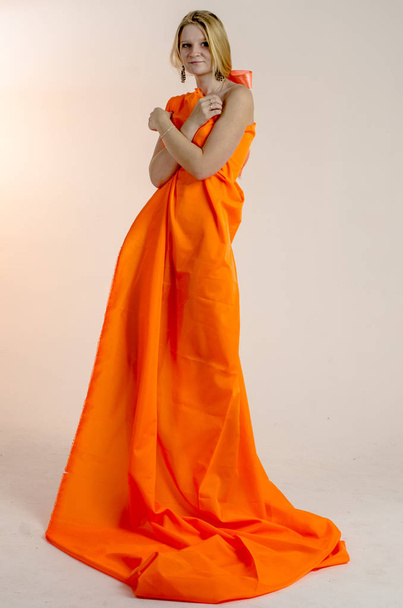 Young beautiful blonde woman in a bright orange fabric in a dress - Foto, Imagem