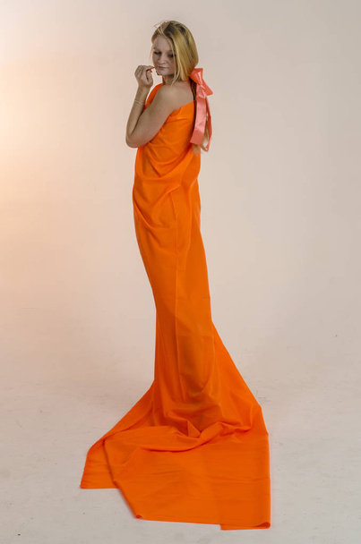 Young beautiful blonde woman in a bright orange fabric in a dress - Zdjęcie, obraz