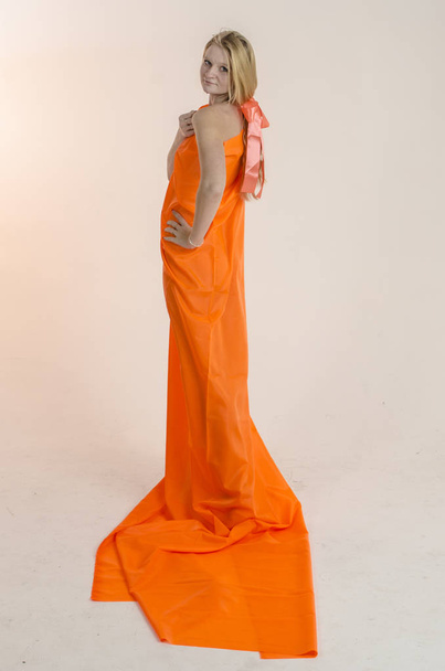 Young beautiful blonde woman in a bright orange fabric in a dress - Фото, зображення