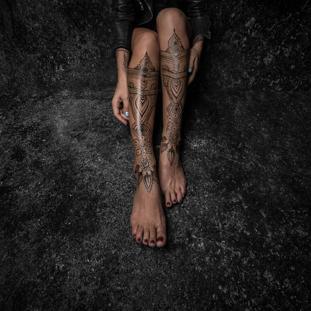 Closeup woman legs with henna tattoo over black stone floor - Fotografie, Obrázek