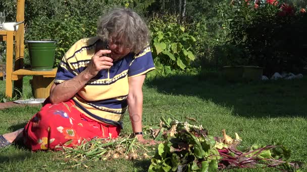 Femme de la campagne senior est assis dans le jardin potager et parler par téléphone cellulaire. 4K
 - Séquence, vidéo