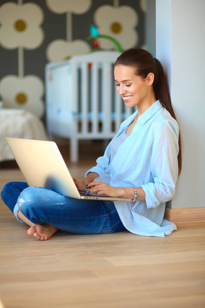 Young beautiful woman at home sitting on the floor with laptop - Фото, изображение