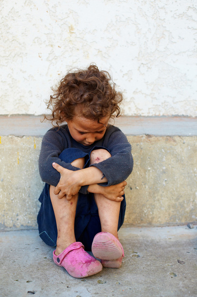 Poor, sad little child girl sitting against the concrete wall - Photo, image