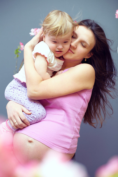 Pregnant loving mother with cute baby girl on hands among pink flowers - 写真・画像