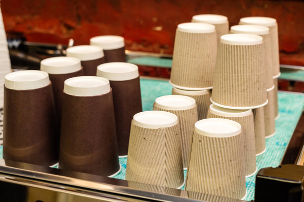 A coffee machine with a large stack of paper cups next to it. - 写真・画像