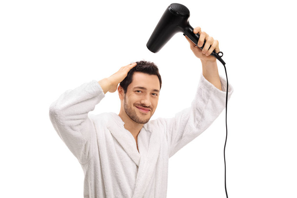 guy in a bathrobe drying his hair with a hairdryer - Фото, зображення