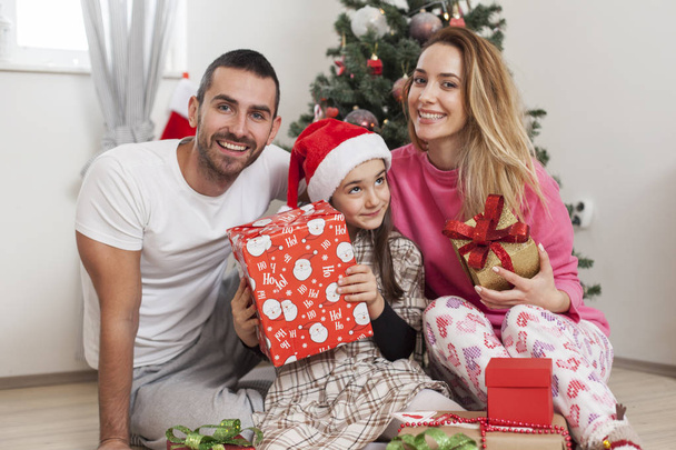 family in front of Christmas tree opening presents - 写真・画像