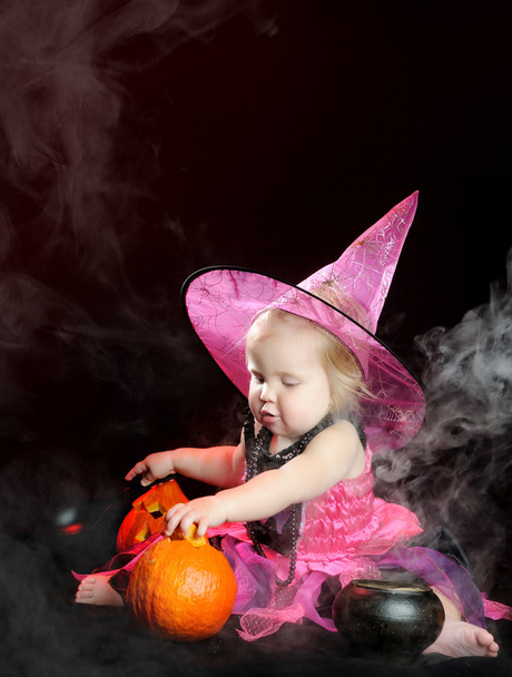 Halloween baby witch with a carved pumpkin over black background - Photo, Image