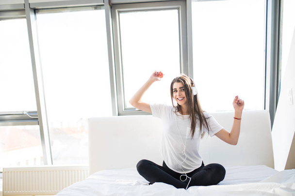 щаслива жінка або дівчина-підліток в навушниках, що слухає музику зі смартфона і танцює на ліжку вдома
 - Фото, зображення