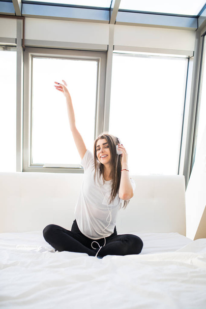 mujer feliz o adolescente en auriculares escuchando música desde el teléfono inteligente y bailando en la cama en casa
 - Foto, Imagen