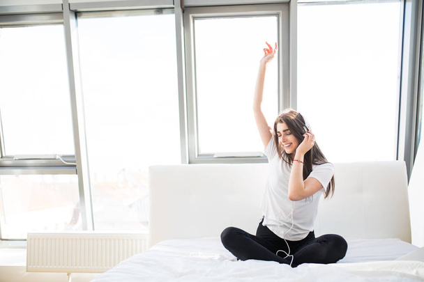 Happy young woman listening to music and singing in bed - Photo, Image