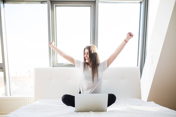 Girl with rised hands in bed using laptop - Photo, Image