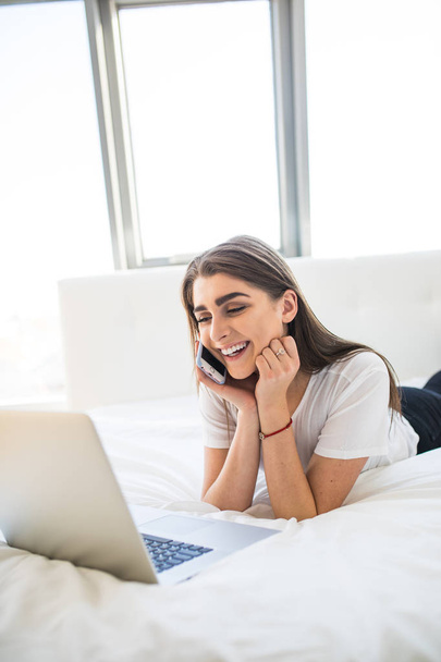 Smiling woman lying down the bed in front of her laptop - Φωτογραφία, εικόνα