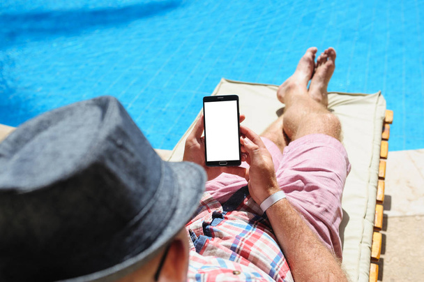 muž v klobouku opalování na telefonu u bazénu - Fotografie, Obrázek