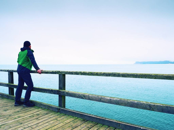 Homem a pensar. Turista em verde na toupeira do mar no corrimão. Névoa de outono
 - Foto, Imagem