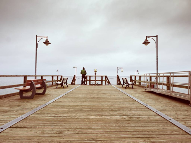 Adult tall man on pier board look over sea to morning fall horizon. Smooth water level  - Photo, Image