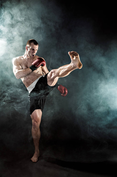 Muscular kickbox or muay thai fighter punching in smoke. - Foto, Imagem