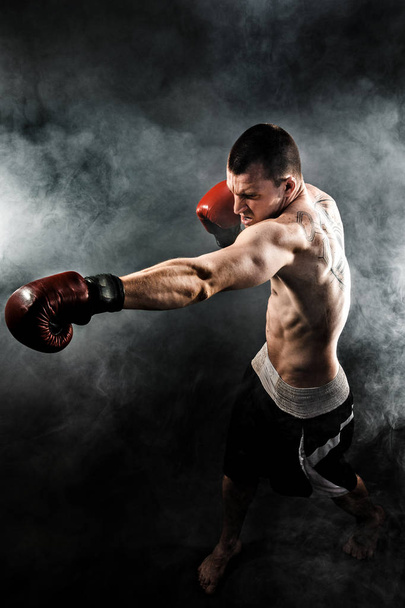 Muscular kickbox or muay thai fighter punching in smoke. - Fotografie, Obrázek