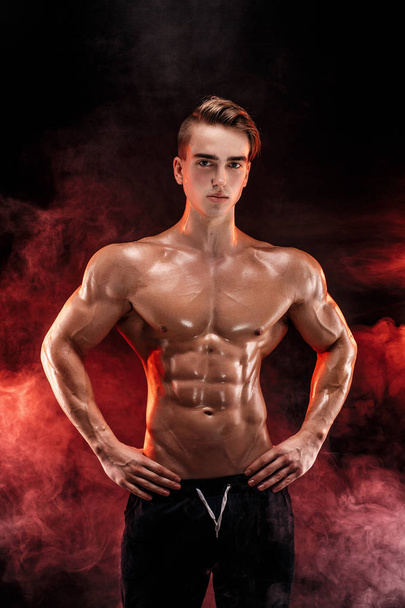 Strong bodybuilder man with perfect abs, shoulders, biceps, triceps, chest posing in smoke hands up. - Foto, Imagem
