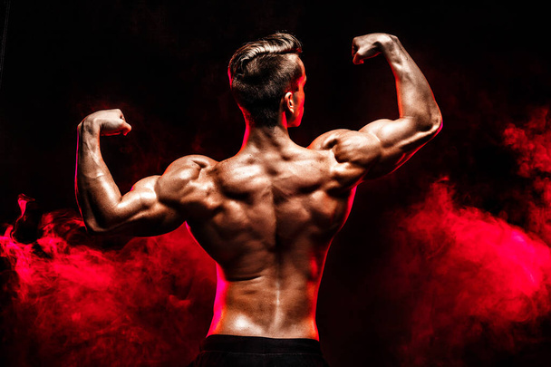 Back view of Unrecognizable man, strong muscles posing with arms up in smoke. - 写真・画像