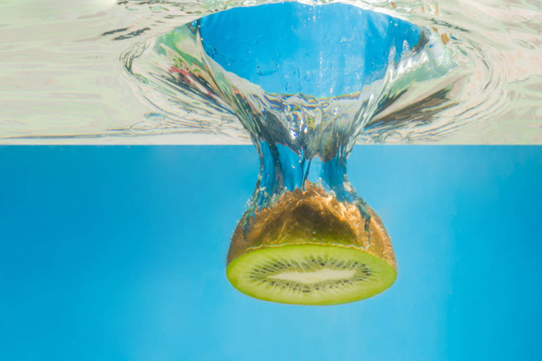 Kiwi splashing in water with blue background - Foto, afbeelding